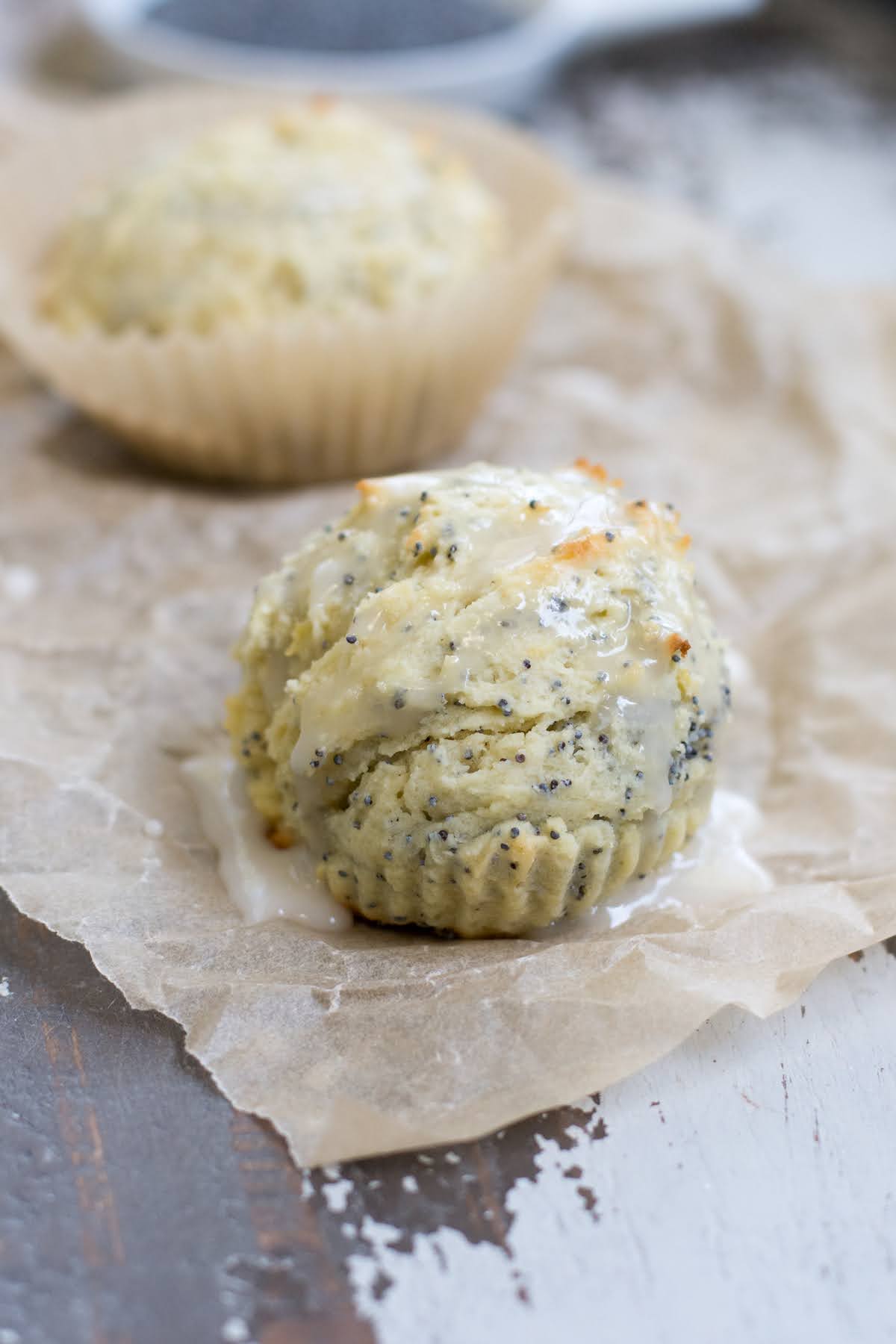 These are the perfect Gluten Free Lemon Poppyseed Muffins. Real lemon and crunchy poppy seeds in a tender, sweet muffin. Easy to make! Iced gluten free lemon poppyseed muffins on a piece of parchment.