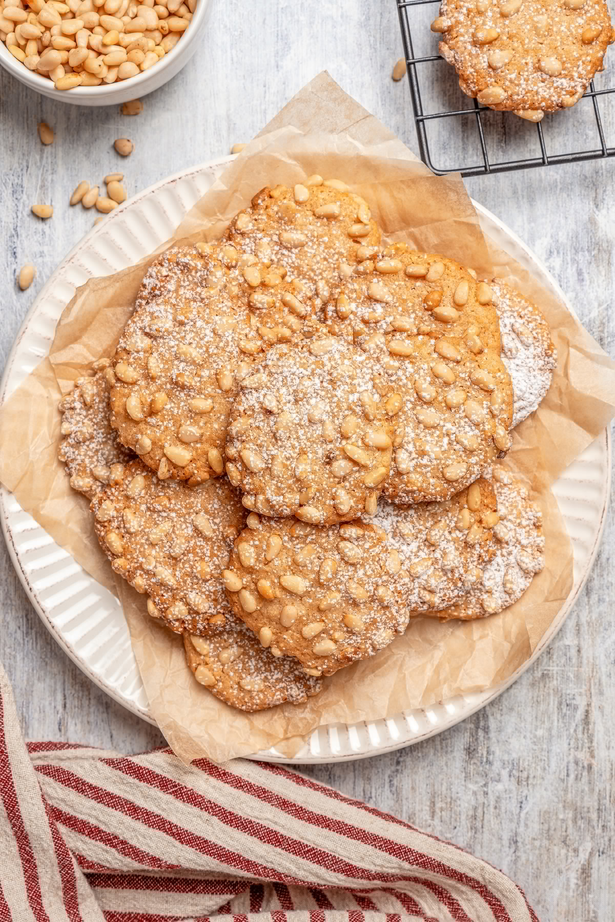 Italian Pignoli Cookies are crispy, chewy and almond-y, topped with rich, creamy pine nuts. They're sure to become a family favorite! A plate of pignoli cookies, dusted with powdered sugar.