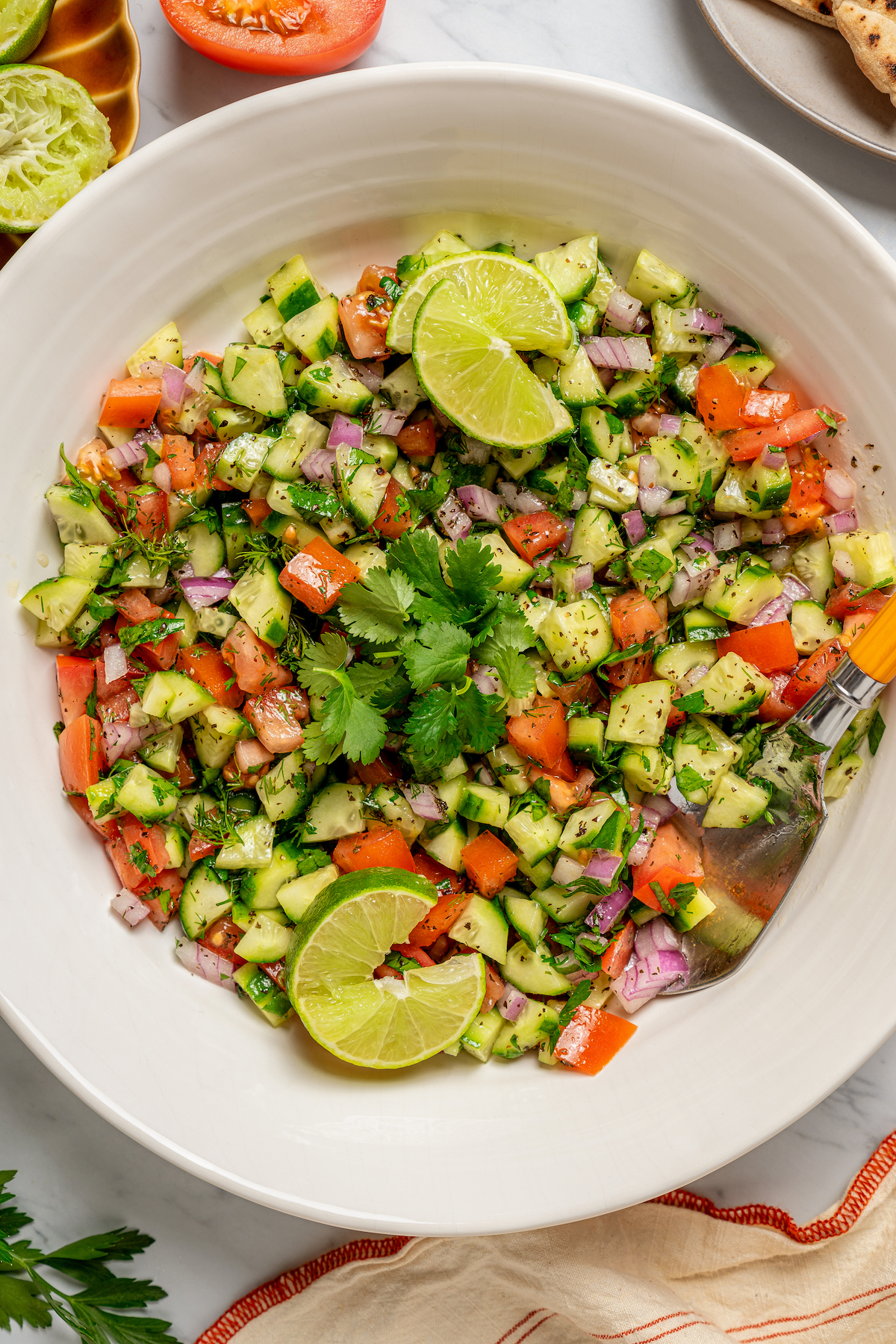 This quick shirazi salad with cucumbers, tomatoes, red onions, and a light vinaigrette is a refreshing Middle Eastern side you'll love. Bowl of shirazi salad with lime wedges.