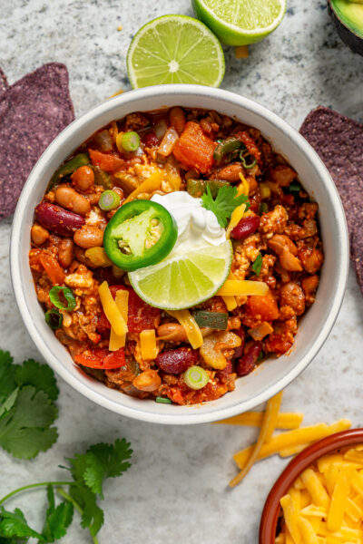 Bowl of turkey chili with a dollop of sour cream, fresh jalapeño, and a lime wedge on top.